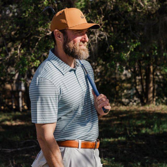 Man in a striped polo shirt and cap holding a golf club outdoors.