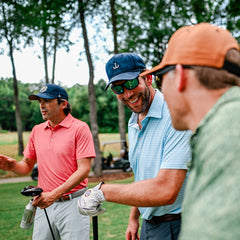 Golfers in performance polos laughing on the tee box. 