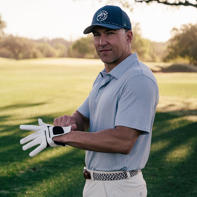 Man on a golf course wearing a blue cap, light blue shirt, and white shorts, holding a golf club.