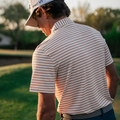 Man in a striped shirt and cap holding a golf club on a golf course