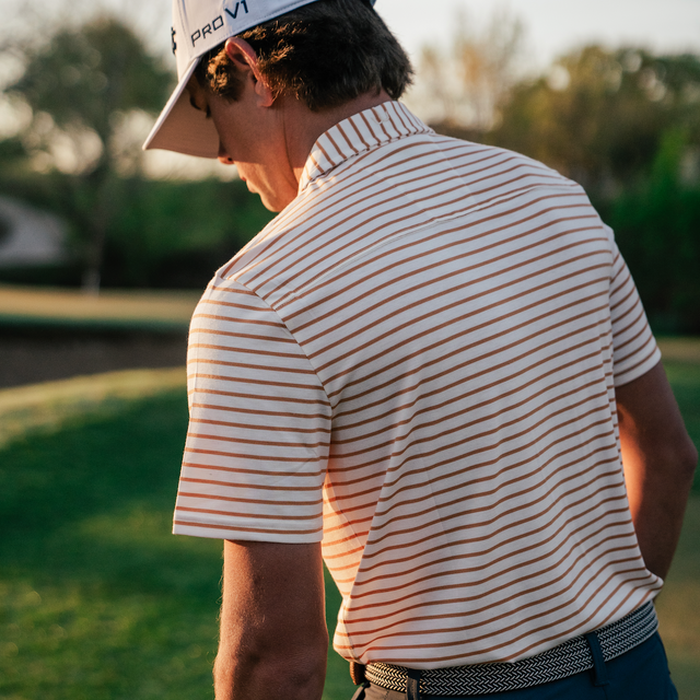 Man in a striped shirt and cap holding a golf club on a golf course