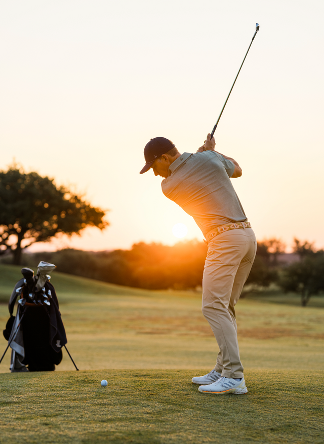 Golfer in pants and green polo hitting approach shot