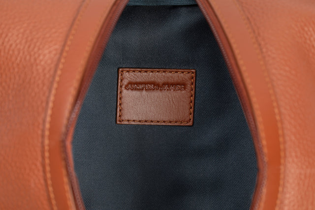 Close-up of a brown leather label on a black fabric background with orange leather trim.