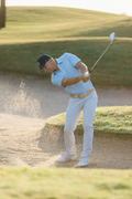 Golfer hitting out of a sand trap on a golf course in pants and performance polo 