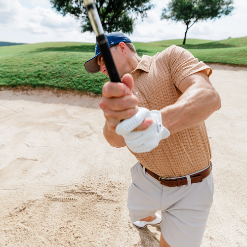 Man in a golf course, preparing to hit a golf ball with a club.