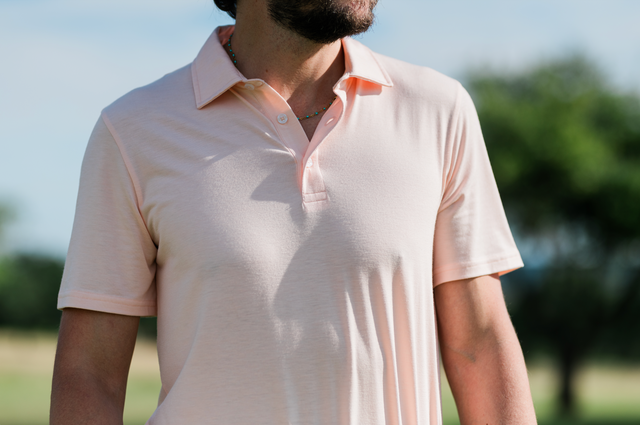 Man wearing a light pink polo shirt outdoors with greenery in the background