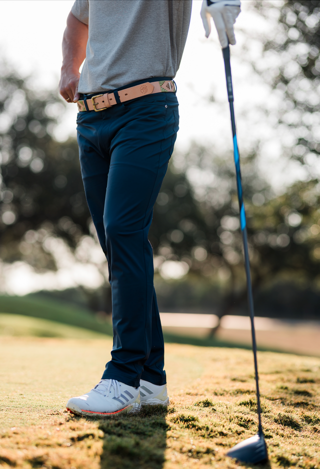 Person on a golf course holding a golf club, wearing navy pants and white shoes.